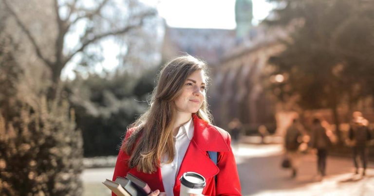 Una chica vestida de rojo, con libros de estudiante en una ciudad extranjera. Representa un seguro de viaje anual. Seguro durante un año. Credito: pexels-olly.
