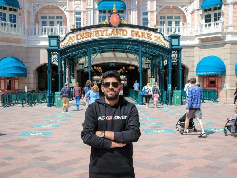 Hombre con chaqueta negra de pie sobre el suelo de hormigón marrón, en disneyland paris francia.