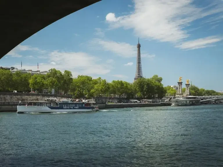 Barco turístico navegando por el río Sena en París con la Torre Eiffel y el puente Alejandro III al fondo en un día soleado.