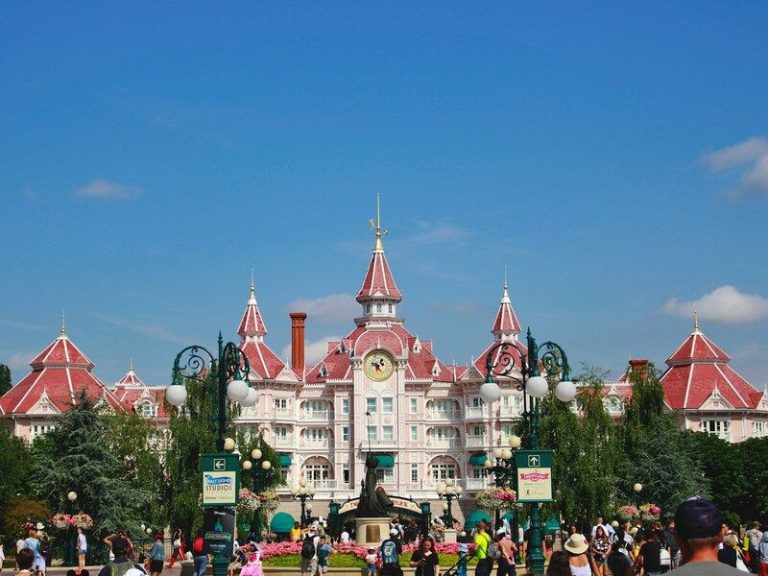 una foto de disneyland paris de dia, se ve un edificio pintoresco rodeado de arboles