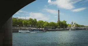 Barco turístico navegando por el río Sena en París con la Torre Eiffel y el puente Alejandro III al fondo en un día soleado.