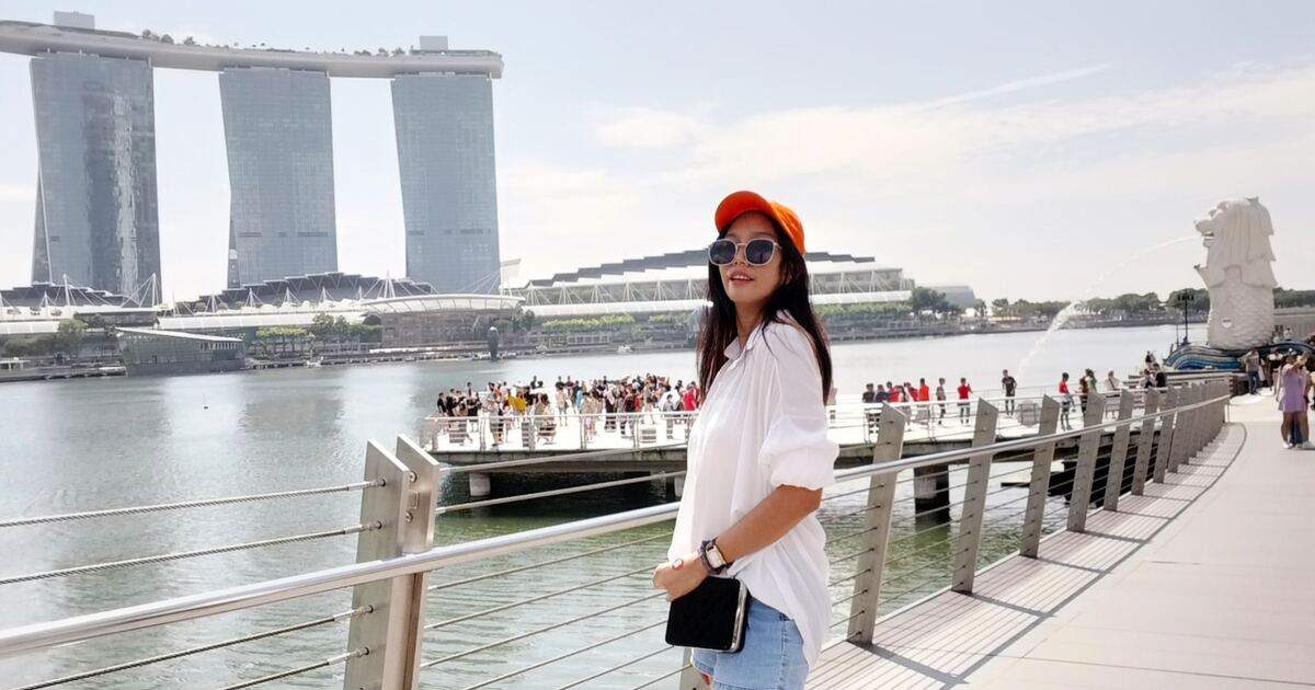 Mujer turista junto a una bahía en Singapur. Es un día soleado, hay personas en un bote. Imagen para representar un seguro de viaje. Credito: abby-dinosaur