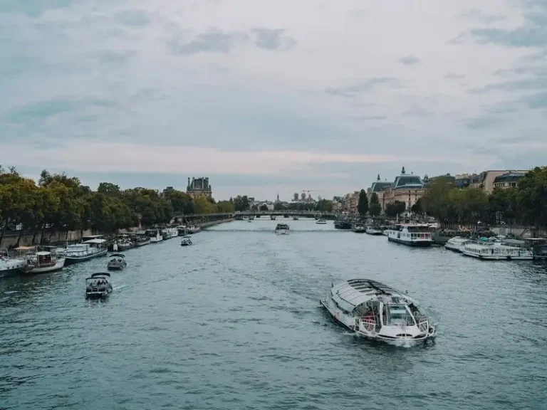 Barco turístico navegando por el río Sena rodeado de embarcaciones y edificios históricos de París bajo un cielo nublado