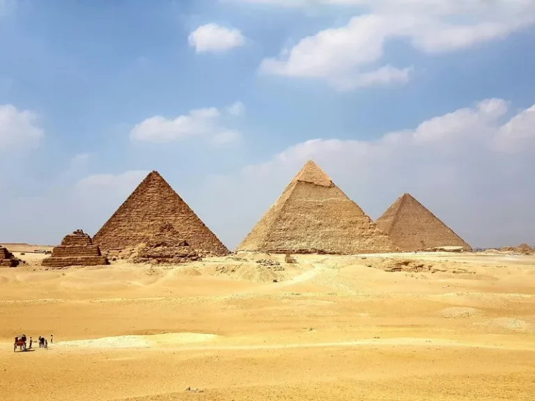 Vista lateral de las tres grandes pirámides de Giza bajo un cielo despejado, mostrando la erosión natural de la piedra caliza.