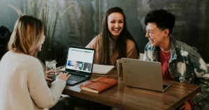 Estudiantes en una mesa de trabajo, con libros, divirtiéndose durante una sesión de estudio. imagen para representar el seguro de estudiantes study plus cobertura europa.