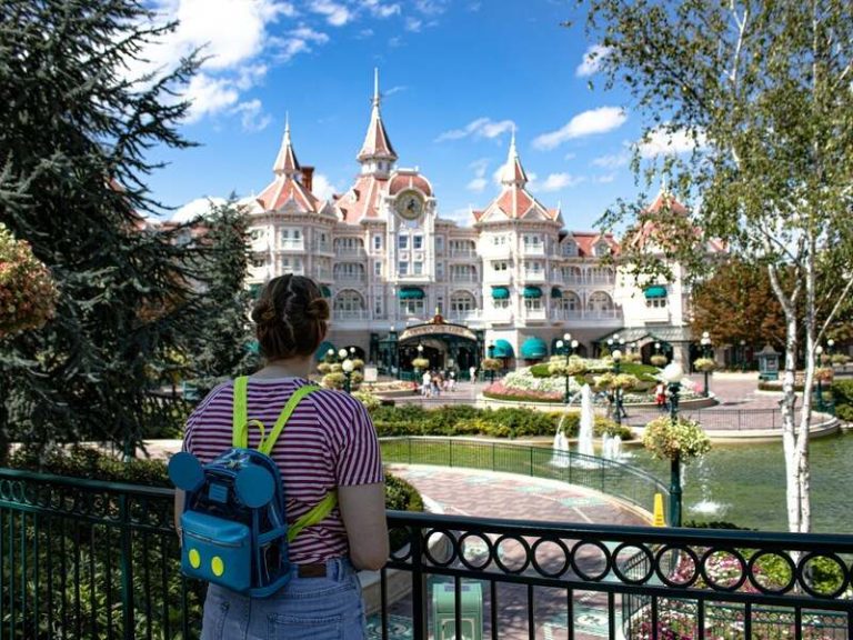 una mujer con camisa de rayas junto a una fuente de dia en disneyland parís