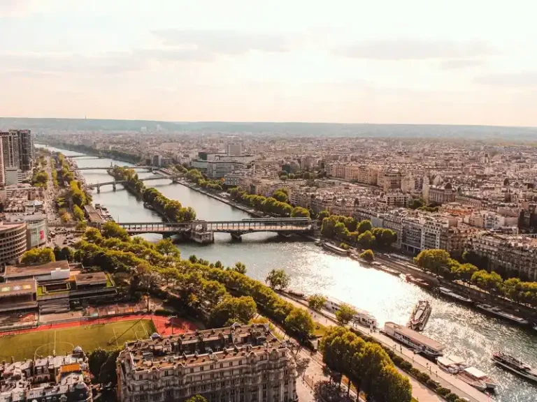 Fotografía aérea del río Sena cruzando la ciudad de París, mostrando sus puentes, la île aux Cygnes y edificios emblemáticos iluminados por la luz cálida del atardecer.